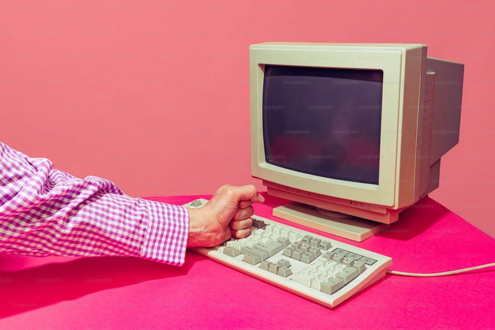 明るいピンクの背景にビンテージコンピュータのモニターとキーボードのカラフルな画像。レトロなポップアート、ヴィンテージのもの、古いものと現代的なもののコンセプト。広告用のスペースをコピーする