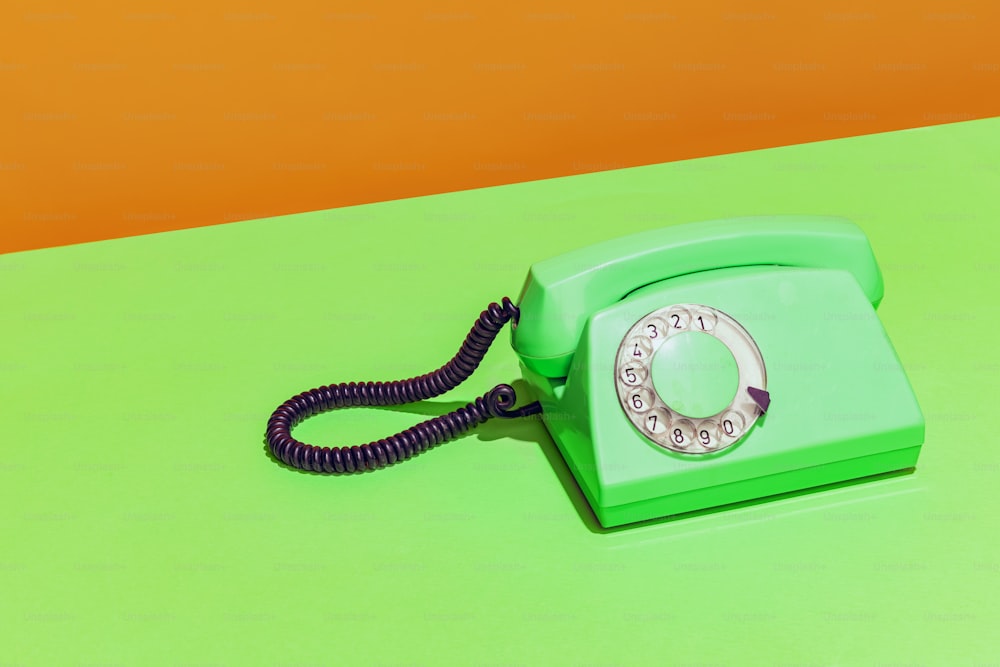 연한 녹색과 주황색 배경에 녹색 네온 복고풍 전화기의 화려한 밝은 이미지. 유선 전화. 팝 아트의 개념, 빈티지 물건, 옛 것과 현대의 혼합. 광고를 위한 복사 공간