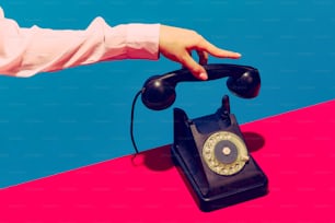 Retro objects, gadgets. Female hand holding handset of vintage phone isolated on blue and pink background. Vintage, retro 80s, 70s style. Complementary colors. Copy space for ad, design