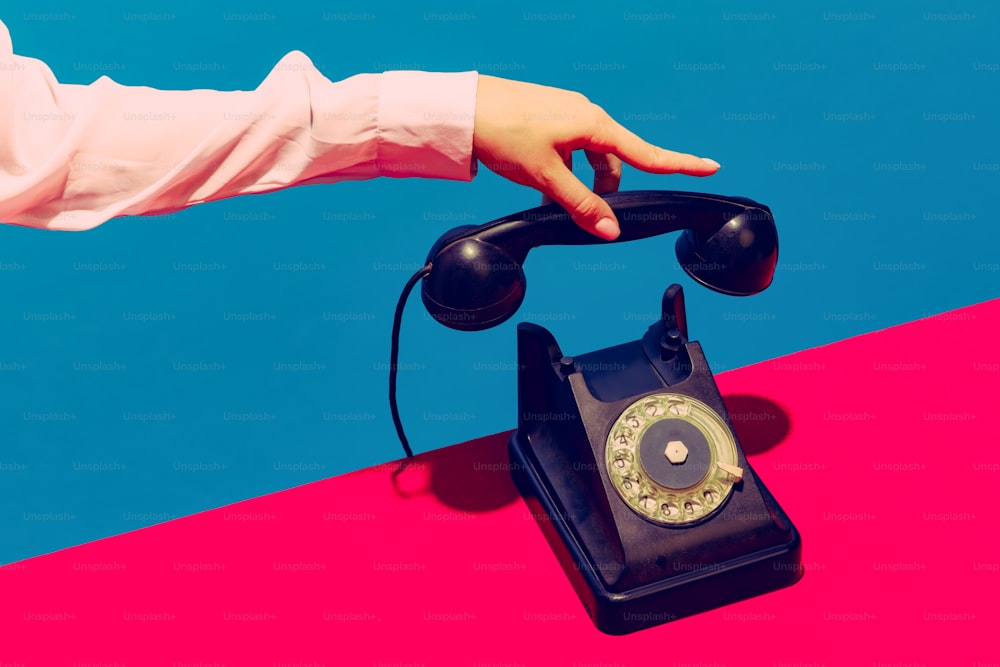 Retro objects, gadgets. Female hand holding handset of vintage phone isolated on blue and pink background. Vintage, retro 80s, 70s style. Complementary colors. Copy space for ad, design
