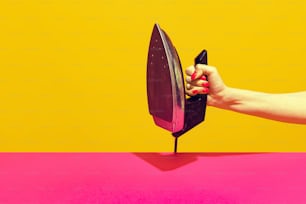 Colorful bright image of female hand holding retro iron isolated over pink yellow background. Collecting vintage things. Concept of retro pop art, mix old and modernity. Copy space for ad