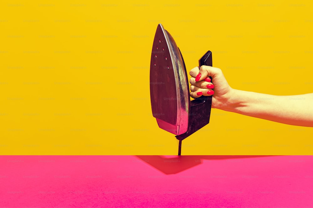Colorful bright image of female hand holding retro iron isolated over pink yellow background. Collecting vintage things. Concept of retro pop art, mix old and modernity. Copy space for ad