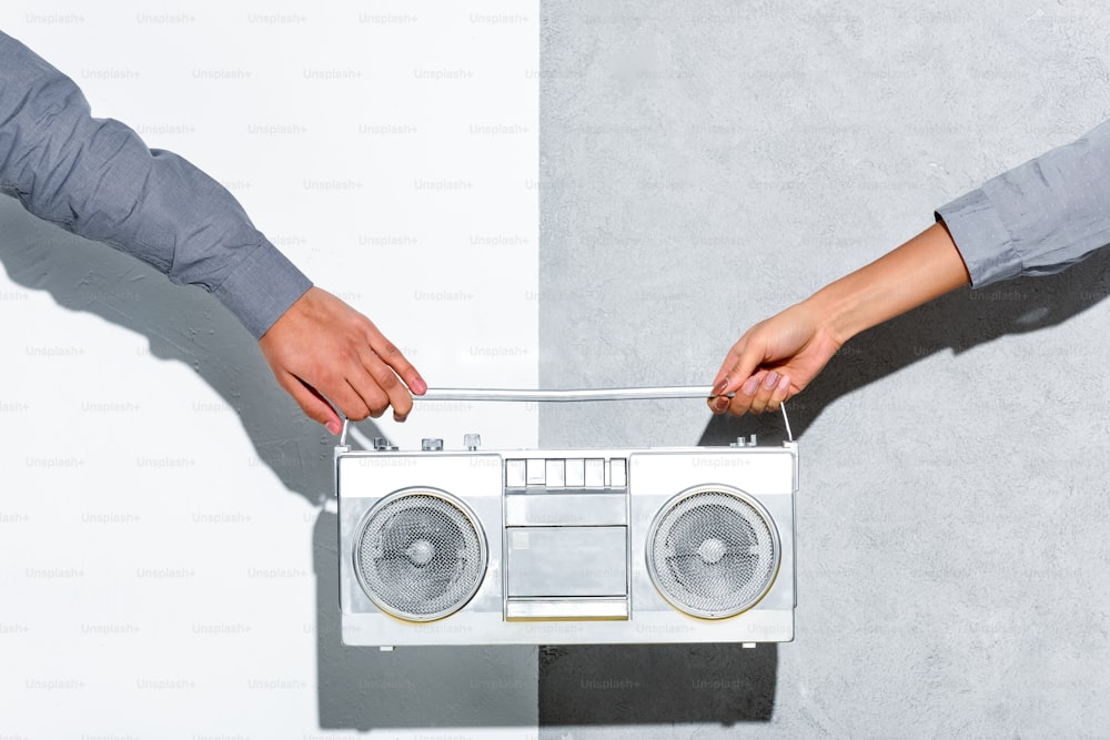 Close-up view of young couple holding boombox in hands on grey and white background