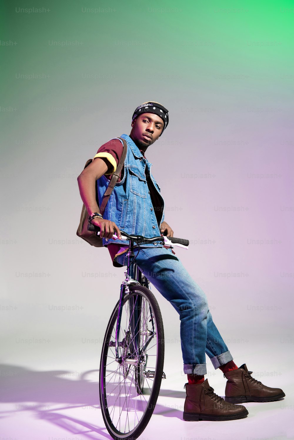 stylish young african american man sitting on bicycle and looking away on grey