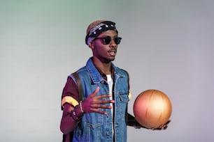 Stilvoller junger Afroamerikaner, der einen goldenen Basketballball auf Grau hält