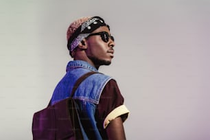 back view of stylish young african american man in sunglasses and leather backpack looking away isolated on grey