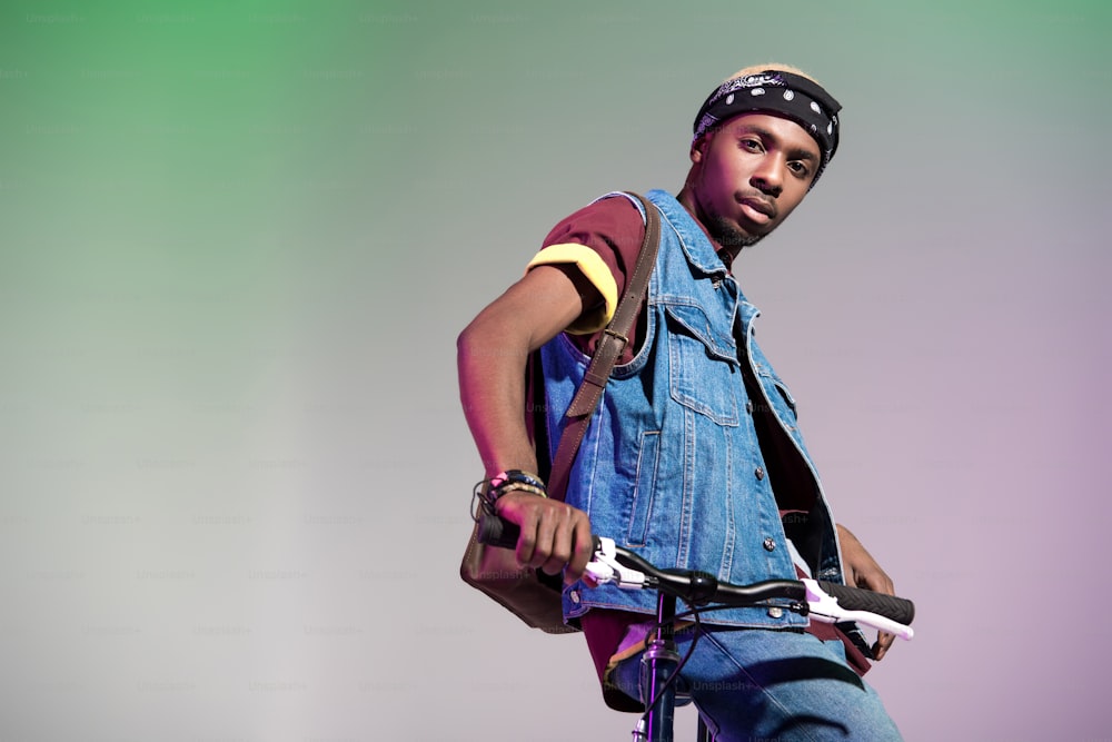 stylish young african american man standing with bicycle and looking at camera isolated on grey