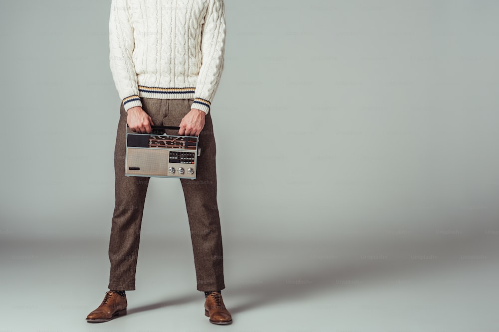 Beschnittenes Bild eines Mannes im Retro-Stil, der ein Vintage-Radio auf Grau hält