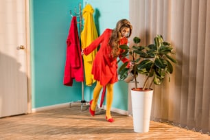 old-fashioned girl in red dress watering plant with watering can at home