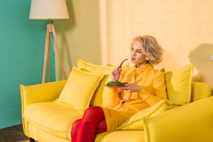 Mujer de estilo retro con brócoli en el plato y chile en la mano descansando en el sofá en Bright Apartment, concepto de casa de muñecas