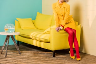 Scatto tagliato della donna in abbigliamento retrò sul divano dell'appartamento colorato, concetto di casa delle bambole
