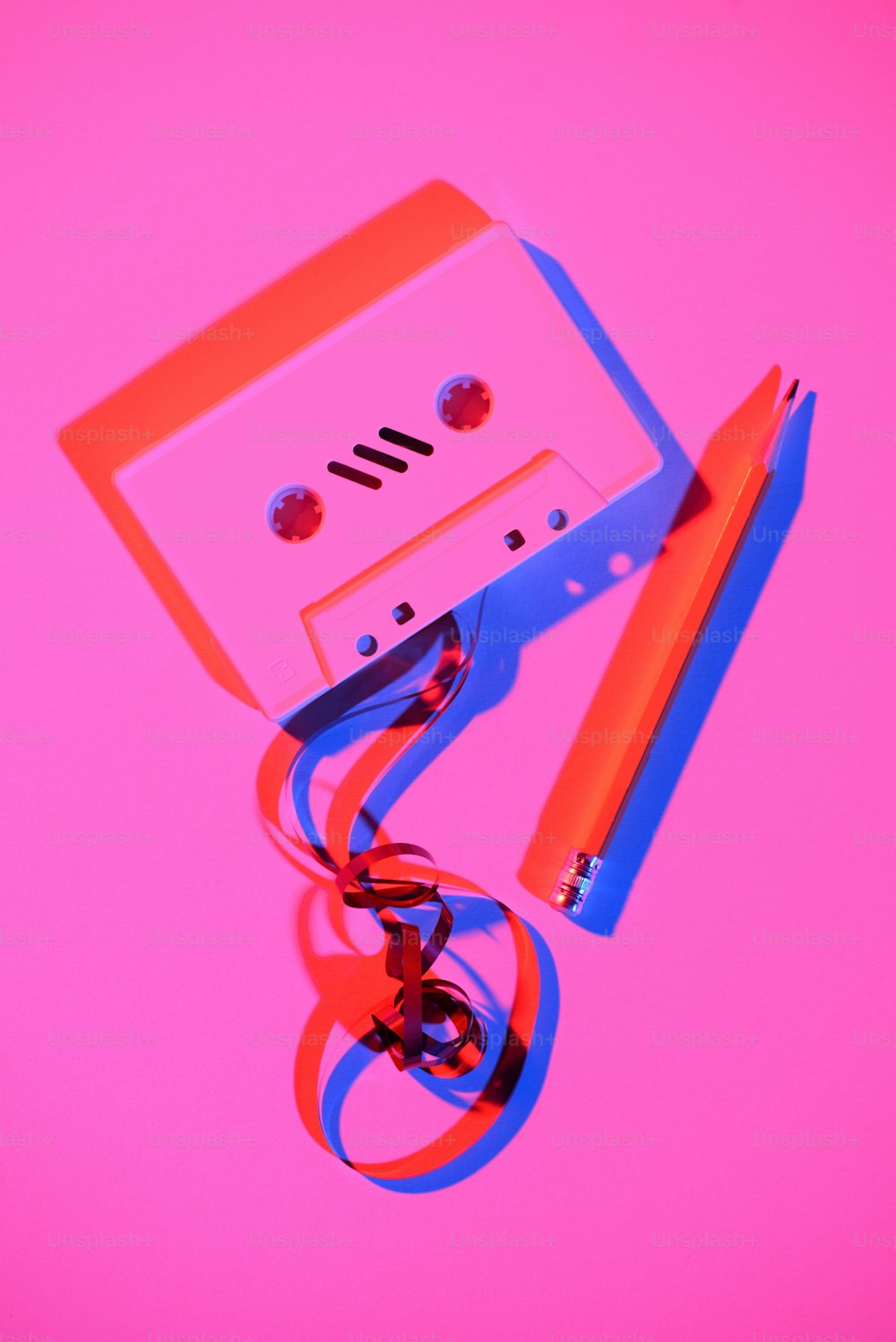 toned pink picture of retro audio cassette with pencil and tape