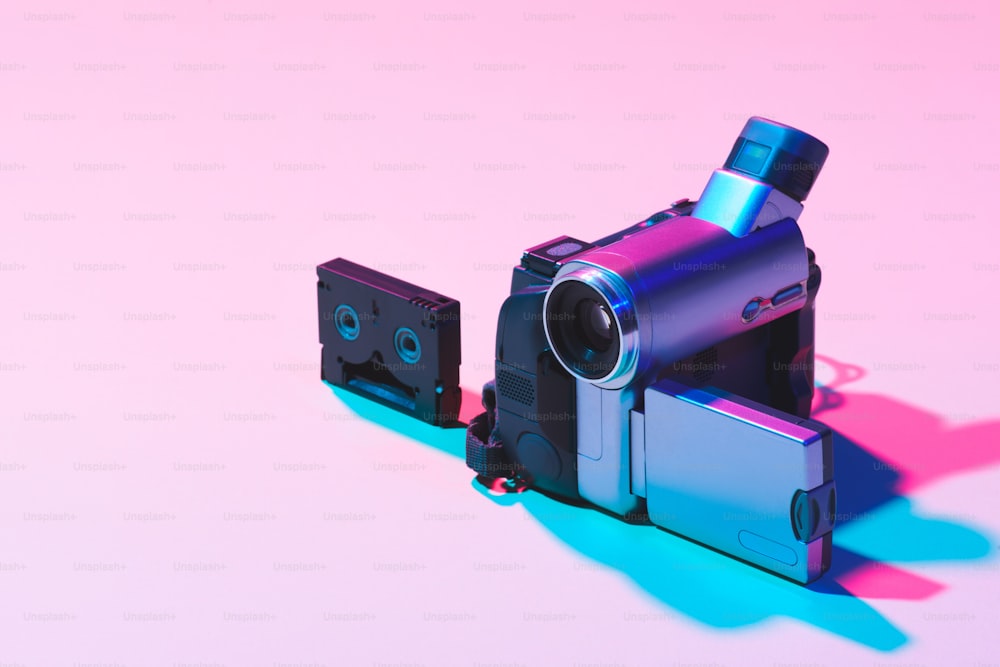 Nahaufnahme der Videokassette und der digitalen Videokamera auf rosafarbenem Hintergrund