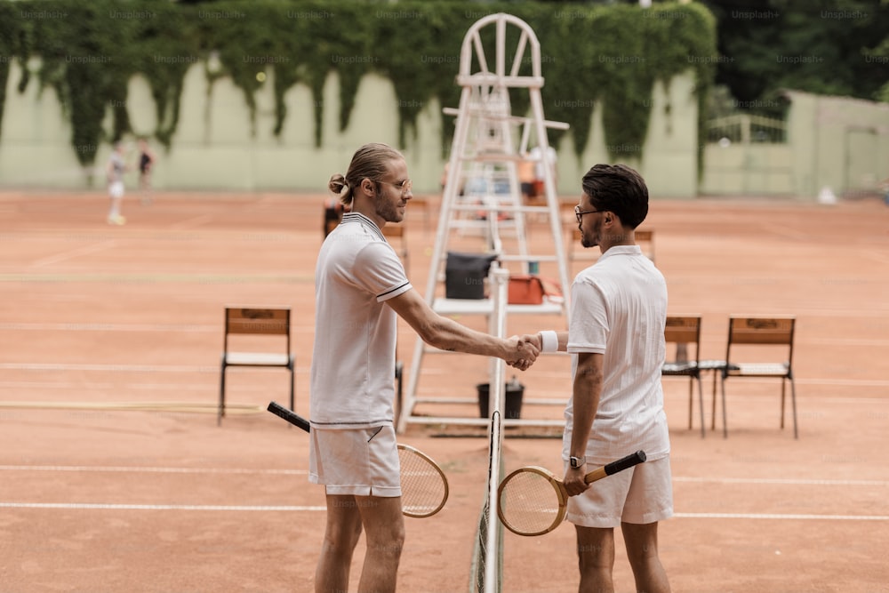 side view of retro styled tennis players shaking hands above tennis net at court