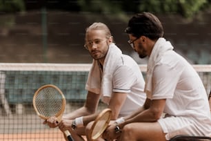 tenistas de estilo retrô sentados em cadeiras com toalhas e raquetes na quadra de tênis