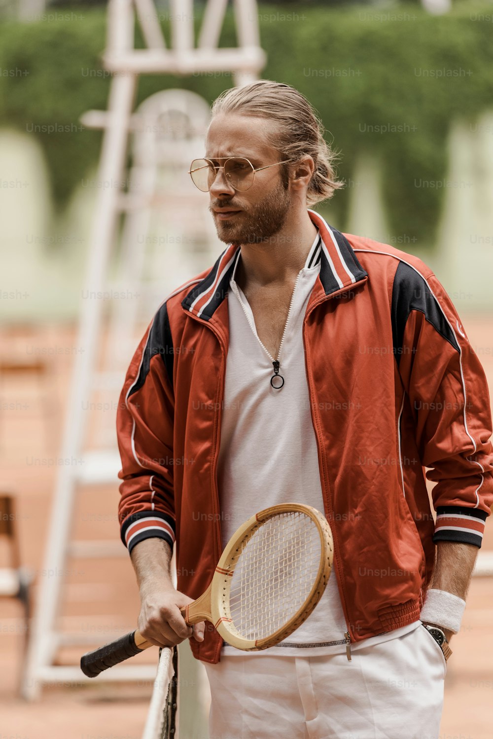 テニスコートでラケットを持って立ち、目をそらすハンサムなレトロスタイルのテニスプレーヤー