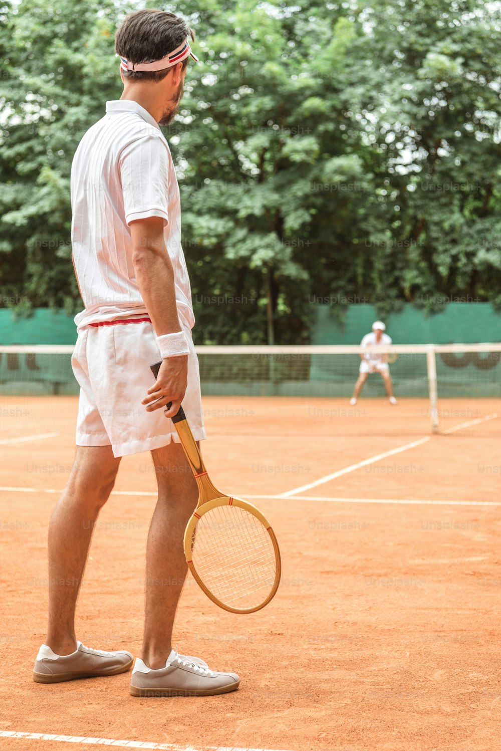 back view of man playing tennis with wooden racket on tennis court