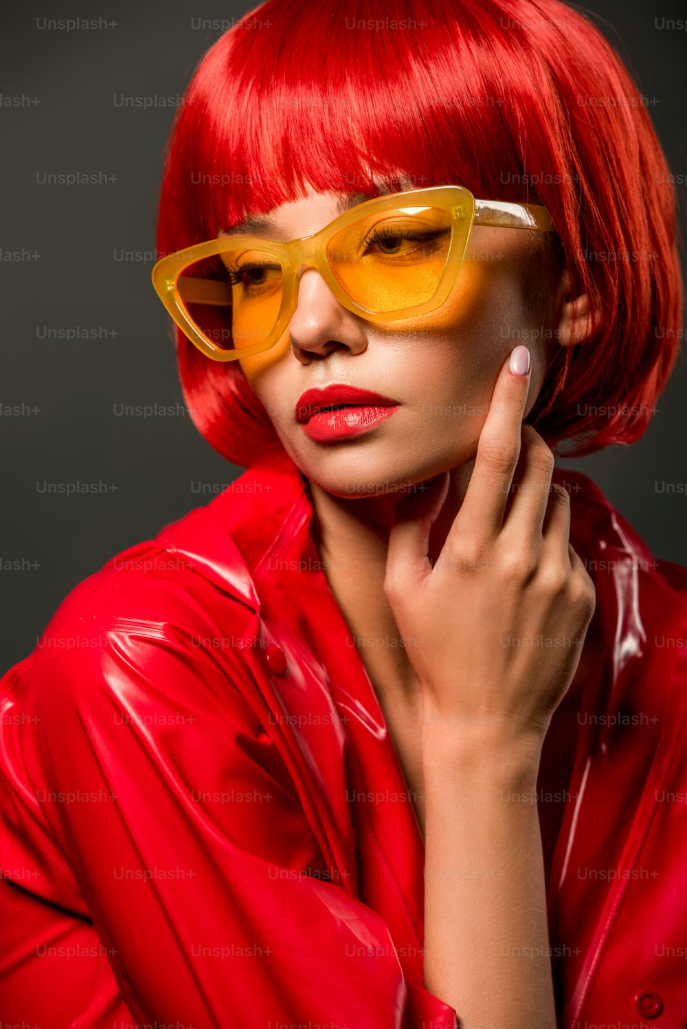Retrato en primer plano de una joven de moda con chaqueta de látex roja y gafas de sol amarillas vintage aisladas en gris