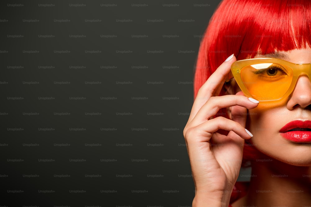 Beschnittene Aufnahme einer schönen jungen Frau mit roten Haaren und einer gelben Vintage-Brille, die isoliert auf Grau in die Kamera schaut