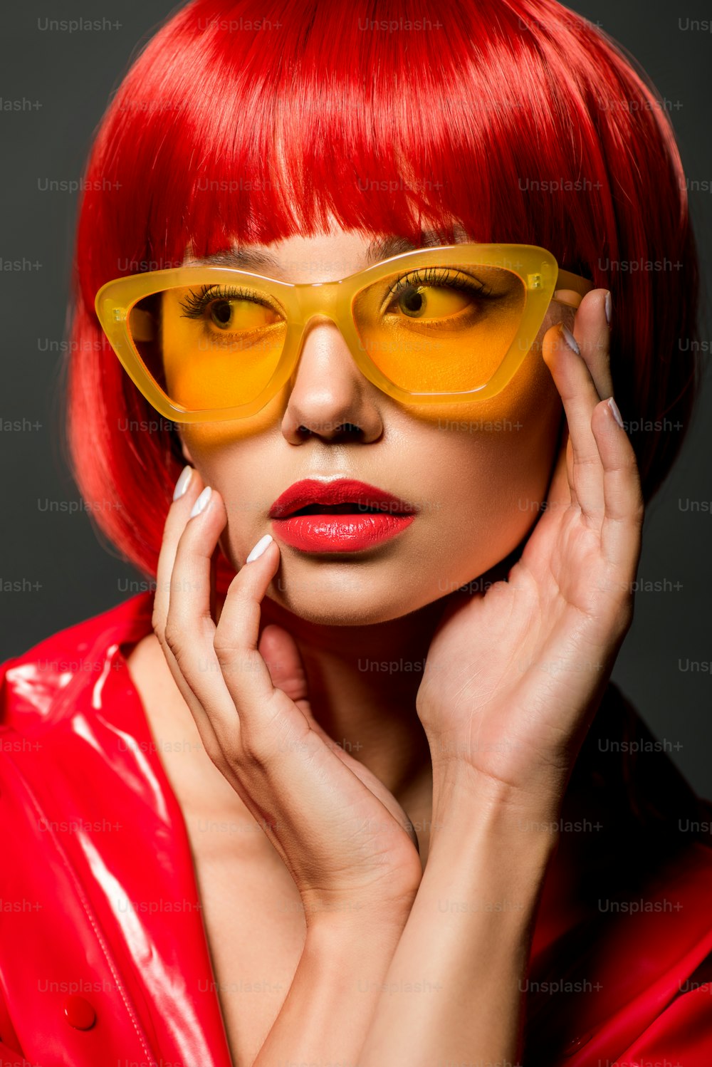Nahaufnahme Porträt einer schönen jungen Frau in roter Latexjacke und gelber Vintage-Sonnenbrille, isoliert auf Grau