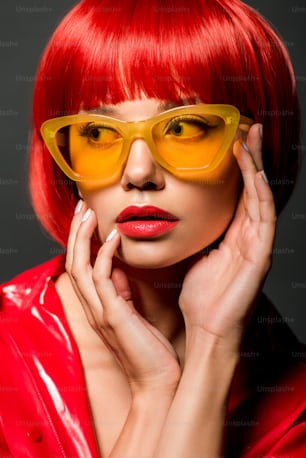 close-up portrait of beautiful young woman in red latex jacket and vintage yellow sunglasses isolated on grey