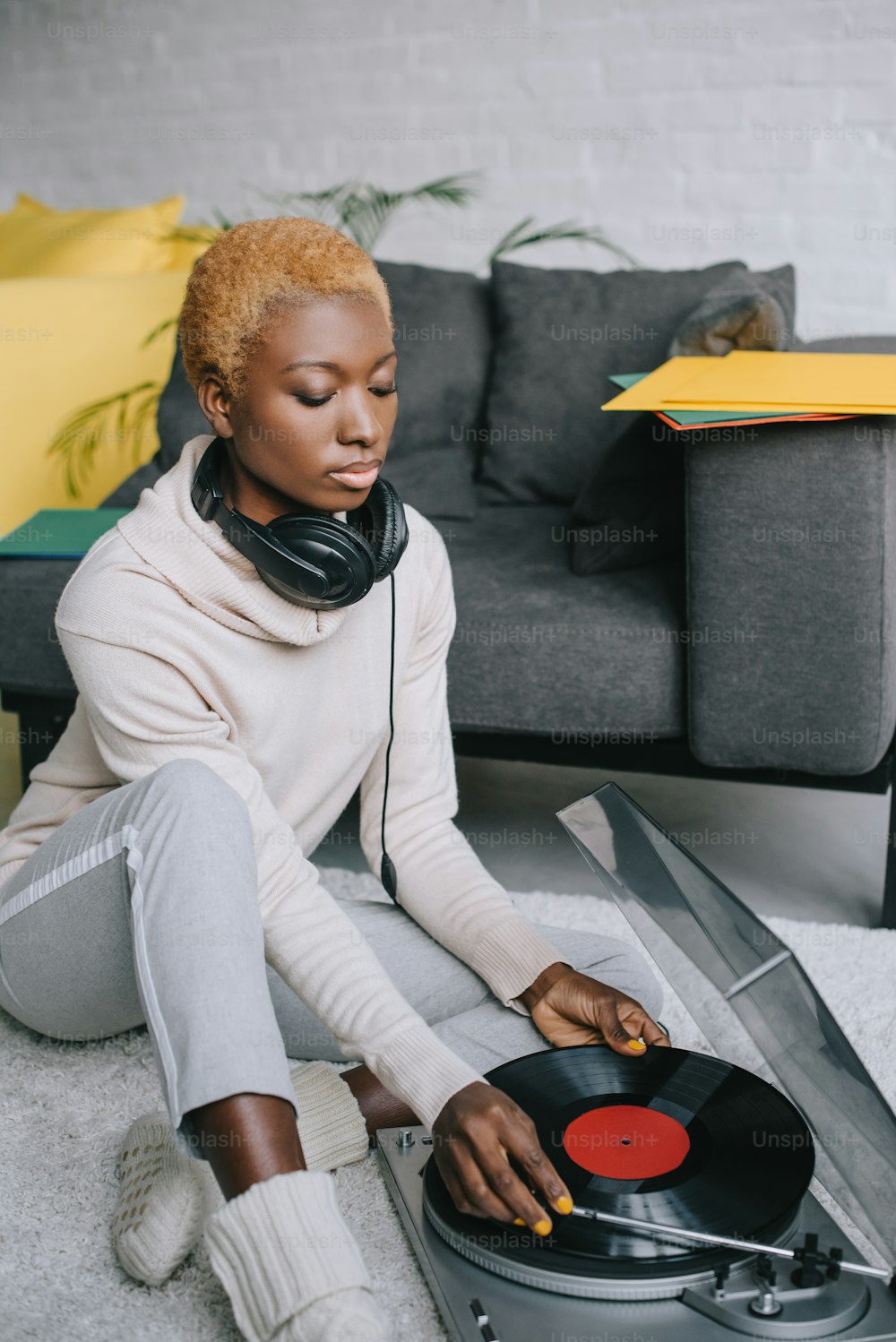 dreamy african american woman sitting on carpet in headphones near record player