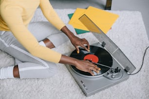 Beschnittene Ansicht einer afroamerikanischen Frau, die einen Plattenspieler auf dem Teppich benutzt