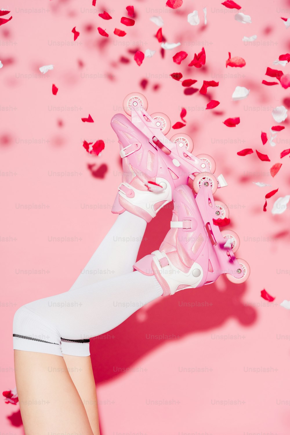 Vista tagliata della ragazza che indossa calze lunghe e pattini a rotelle vicino ai petali di rosa sul rosa