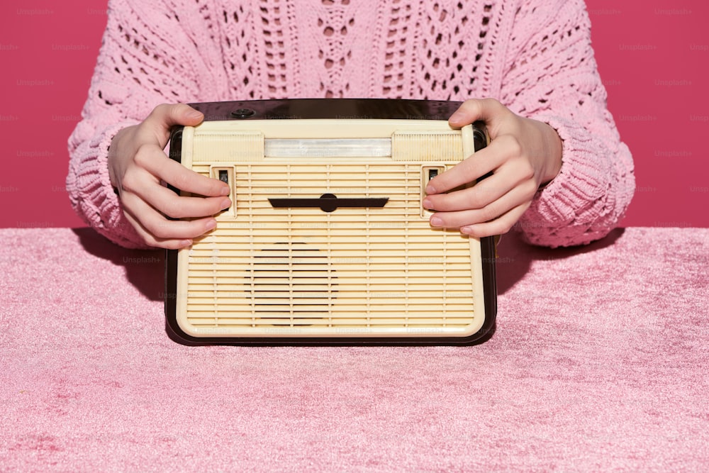 Beschnittene Ansicht einer Frau, die Vintage-Radio auf Veloursstoff hält, isoliert auf rosafarbenem, mädchenhaftem Konzept