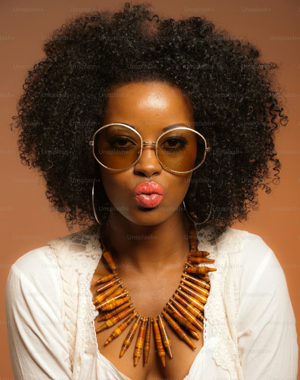 Retro 70s fashion black woman with sunglasses and white shirt. Brown background.