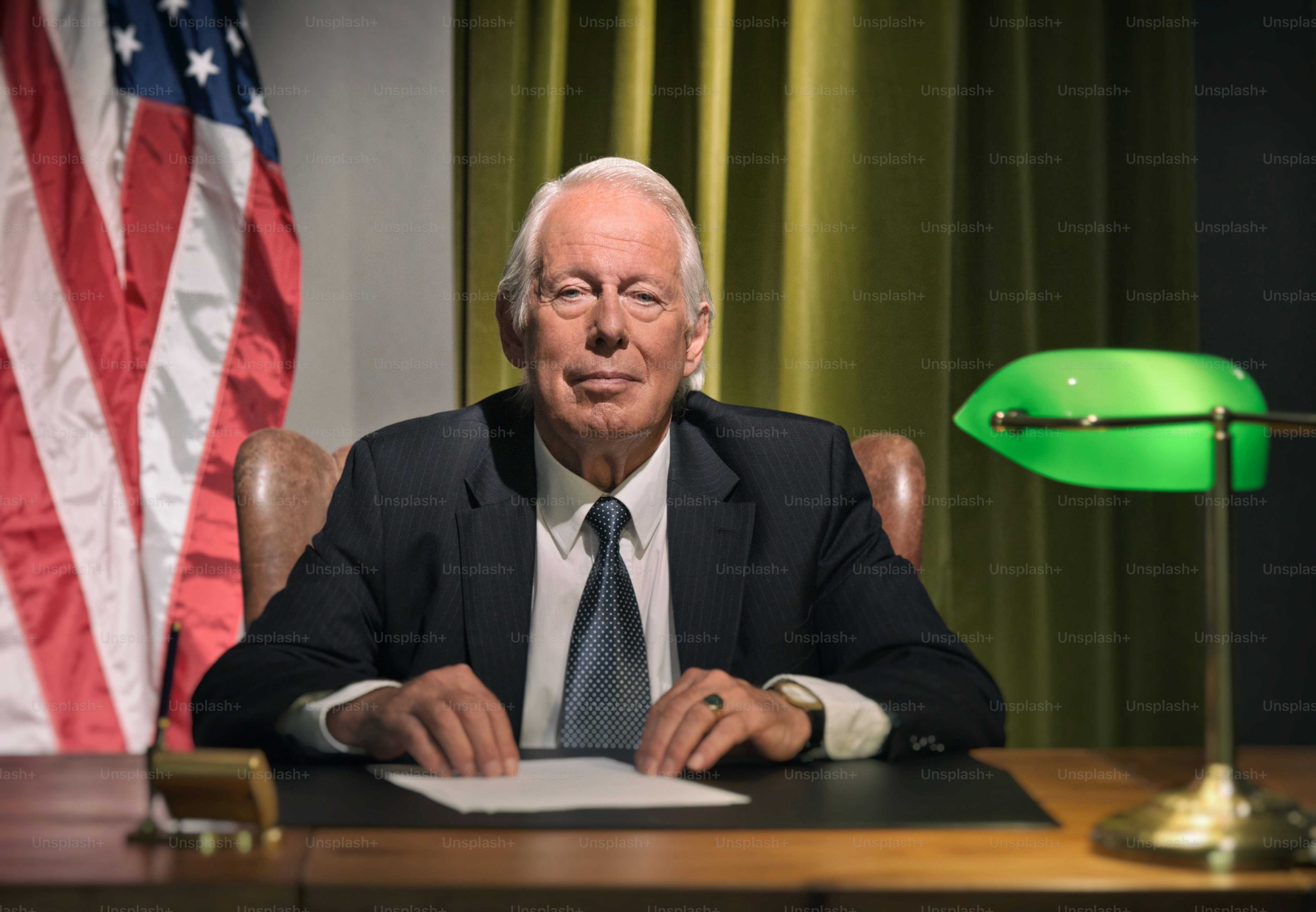 Big boss president sitting behind desk with american flag in the background.