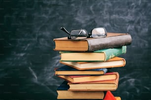 Education concept. Old books and eye glasses on blackboard background