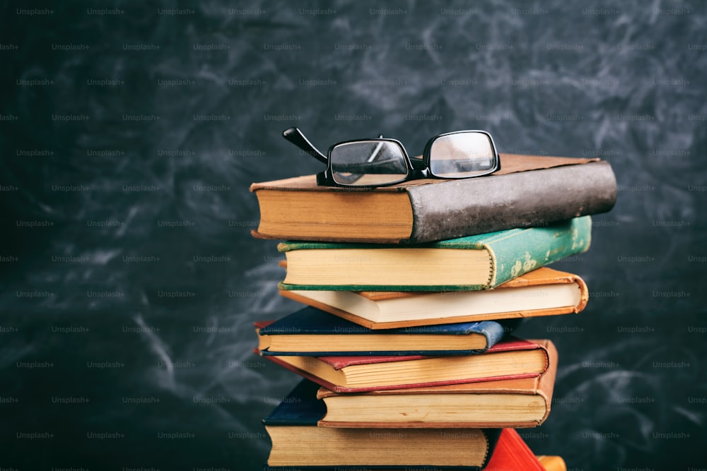 Education concept. Old books and eye glasses on blackboard background