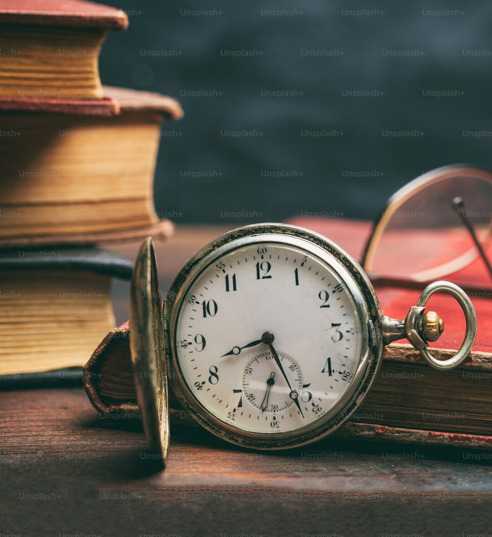 Vintage pocket watch and old books on a wooden office desk background. Time, science concept