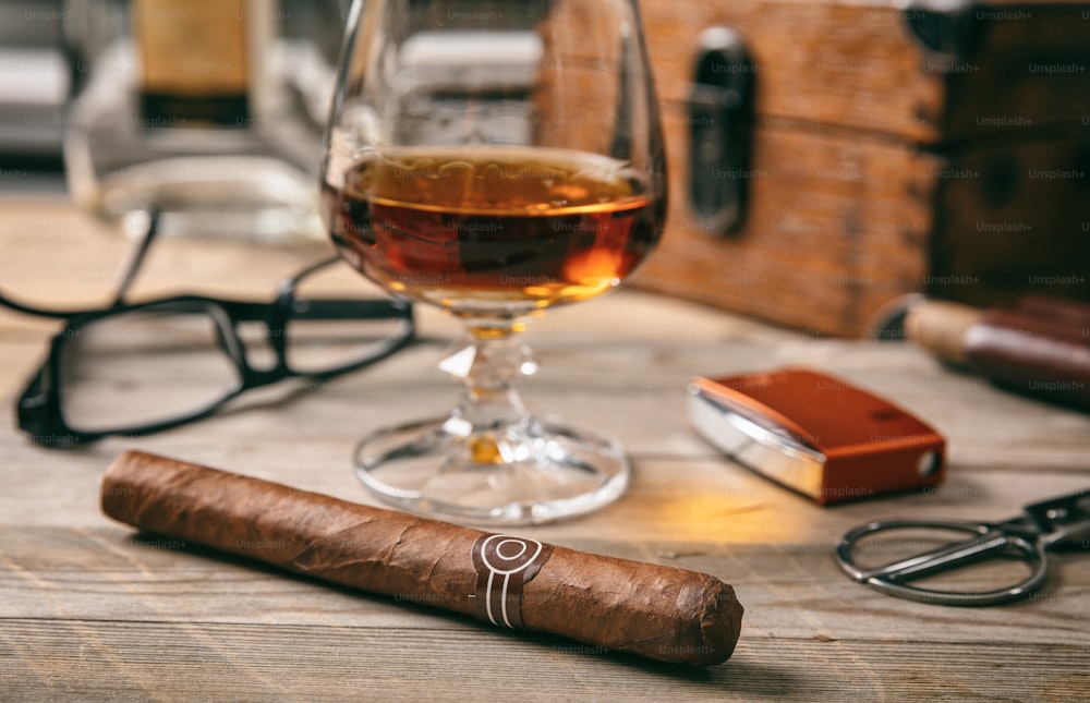 Cuban cigar and a glass of cognac brandy on wooden background, closeup view with details