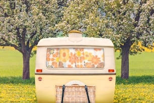 Vintage rear of a caravan in two tone yellow and white in front of a Dutch landscape with blooming flowers and blossoming trees