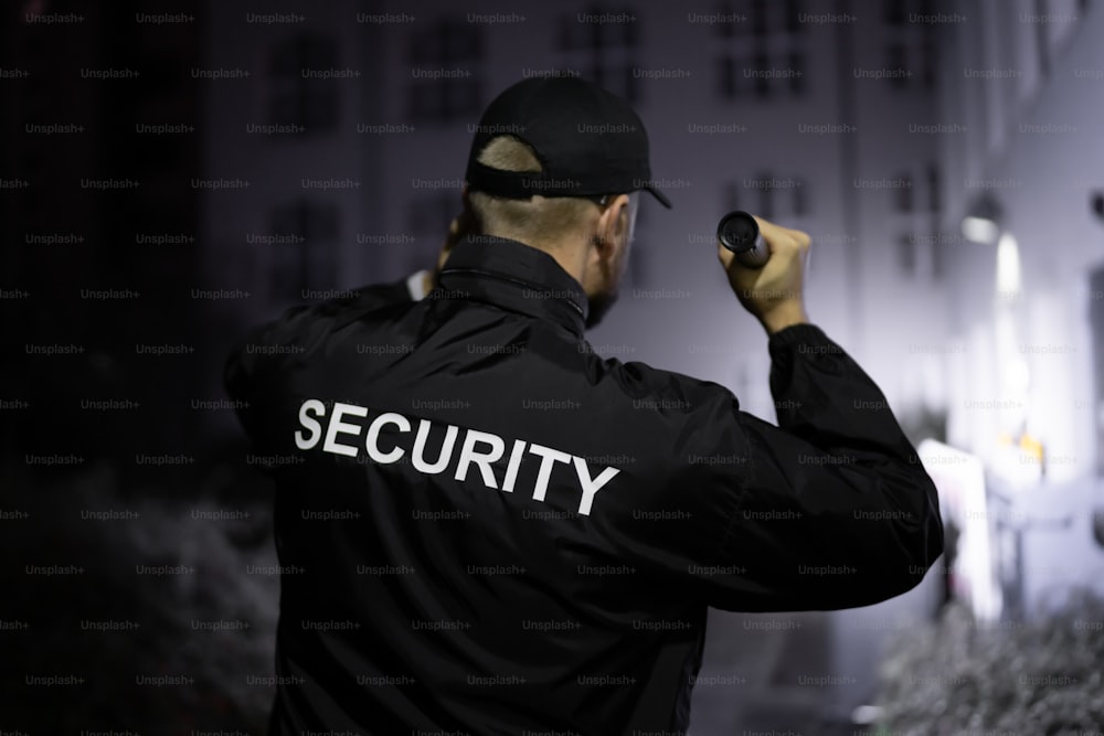 Security Guard Walking Building Perimeter With Flashlight At Night