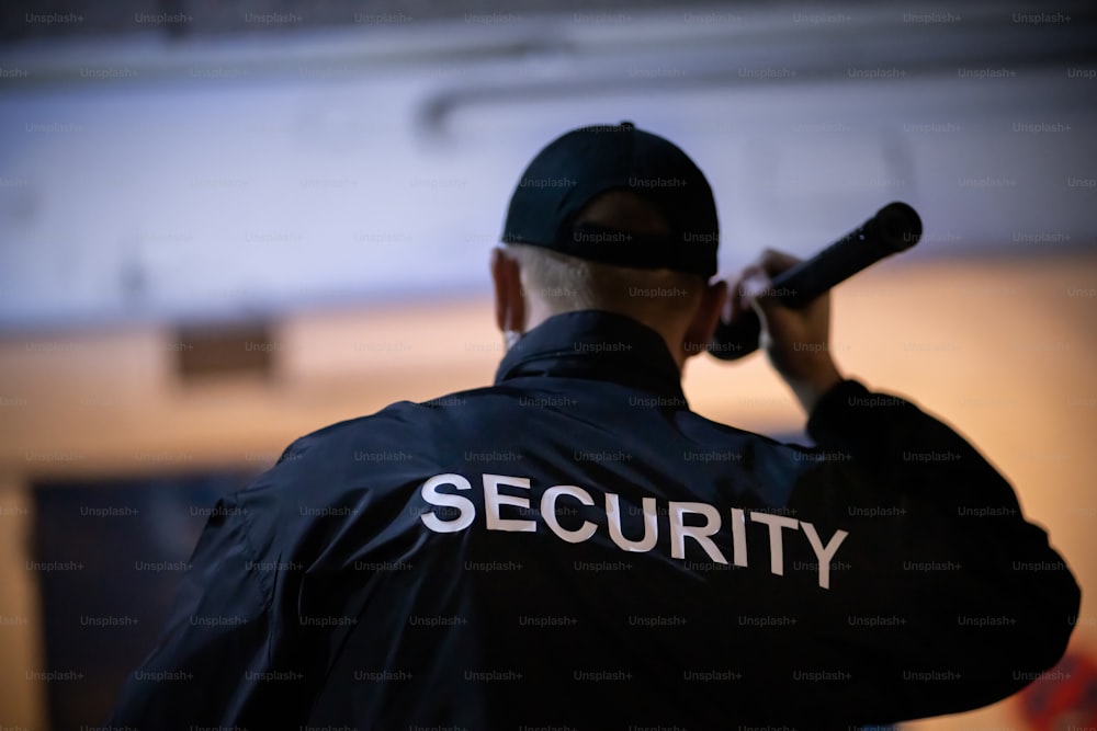 Security Guard Walking Building Perimeter With Flashlight At Night