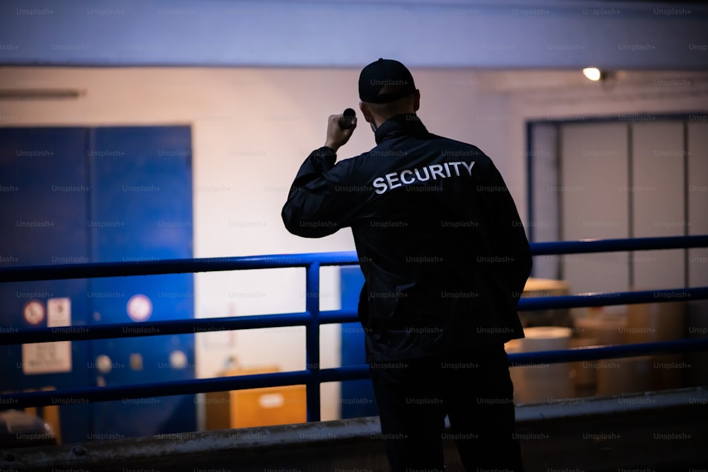 Security Guard Walking Building Perimeter With Flashlight At Night