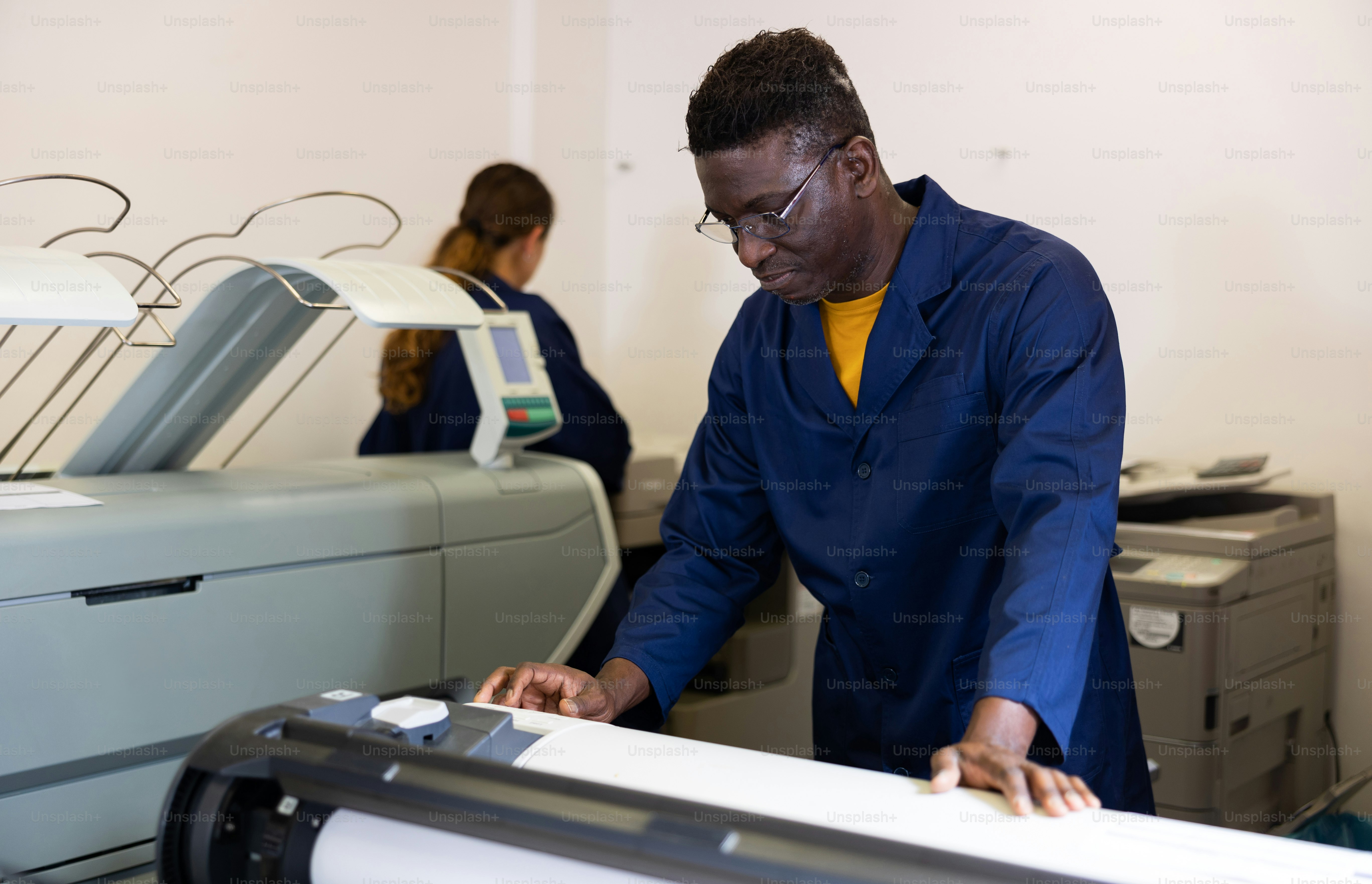 Positive middle-aged African American man in uniform using plotter during work in the printing office