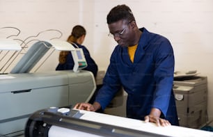 Positive middle-aged African American man in uniform using plotter during work in the printing office