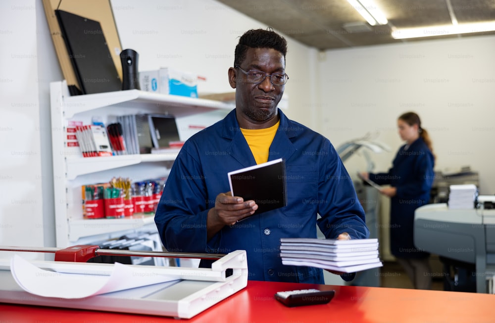 Portrait of friendly male employee of printing house with a stack of notebooks in her hands