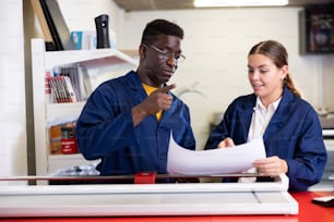 Des collègues multiraciaux heureux vérifient la qualité d’impression et acceptent les épreuves couleur dans l’imprimerie