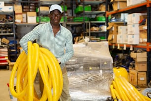 African american man with yellow plastic corrugation for electric cable in large store warehouse