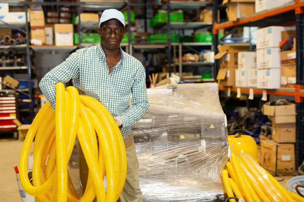 African american man with yellow plastic corrugation for electric cable in large store warehouse