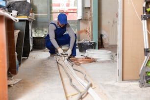 Young civil master working on a construction site indoors is laying a cable on the floor