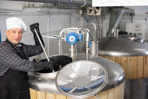 Propietario experto de una pequeña cervecería artesanal que mezcla materias primas en recipiente de fermentación en el taller