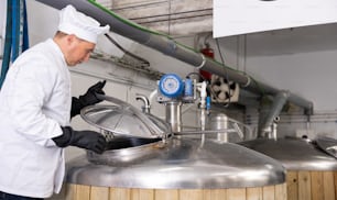 Maître brasseur qualifié concentré ouvrant le couvercle du fermenteur tout en vérifiant le processus de production de bière artisanale en atelier