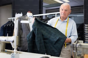 Sastre profesional inspecciona la chaqueta masculina antes de comenzar a trabajar en el taller
