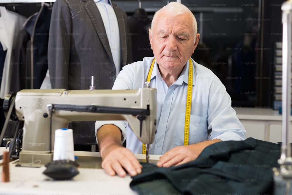 Retrato de un sastre anciano trabajando en una máquina de coser en un estudio